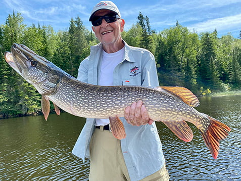 older gentleman displaying big northern pike he caught on the lake